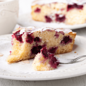 Raspberry and Lemon Frangipane Cake with almond flakes on a white saucer. Recipe from Sam's Recipe Book