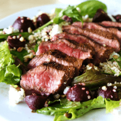 A salad with quinoa, beet and steak garnished with goat cheese