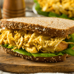 A Coronation Chicken Sandwich with lettuce on a wooden platter