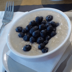 Porridge oats and blueberries served in a white breakfast dish with cutlery on the side