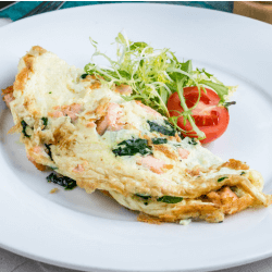 A plate of smoked salmon omelette prepared with cream cheese and chives served with tomatoes and vegetables on a white plate