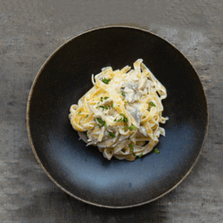 A dish of Stilton Pasta with Spinach and Mushrooms served in a black bowl