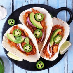 Three Mexican Tacos with chili peppers and onion served on a black plate with lime slices