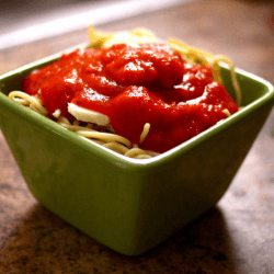 Tomato pasta sauce served with pasta in a green bowl lying on a tabletop