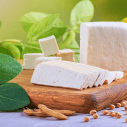 Slices of vegan cheese cut from a block of cheese on a wooden board