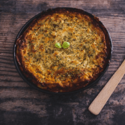 A Zucchini Lasagna dish in a black casserole on a wooden table with a wooden serving spoon on the side