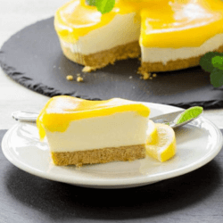 A slice of lime and lemon cheesecake on a white dessert plate with the remainder of the cheesecake in the background