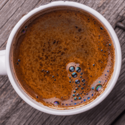 A white cup of spiked coffee spiked with Kahlua coffee liqueur set on a wooden background